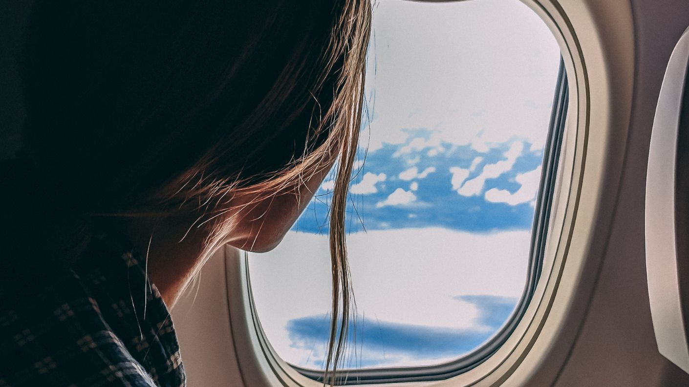 Donna che guarda fuori dal finestrino di un aereo, con vista sulle nuvole, simbolo di viaggio e avventura aerea.