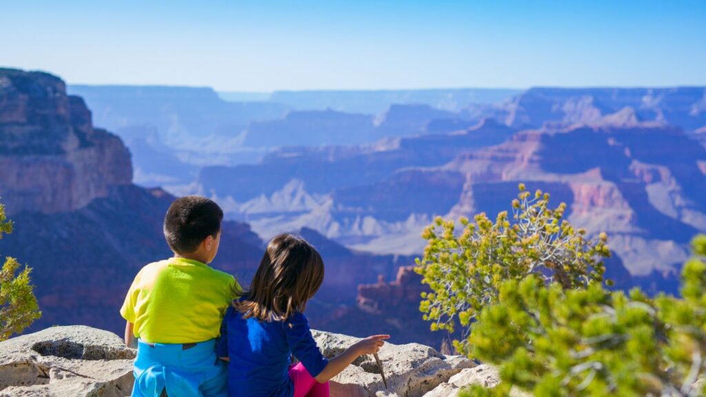Due bambini di spalle che ammirano un panorama di rocce e montagne, simbolo di avventura e viaggi in famiglia nella natura.