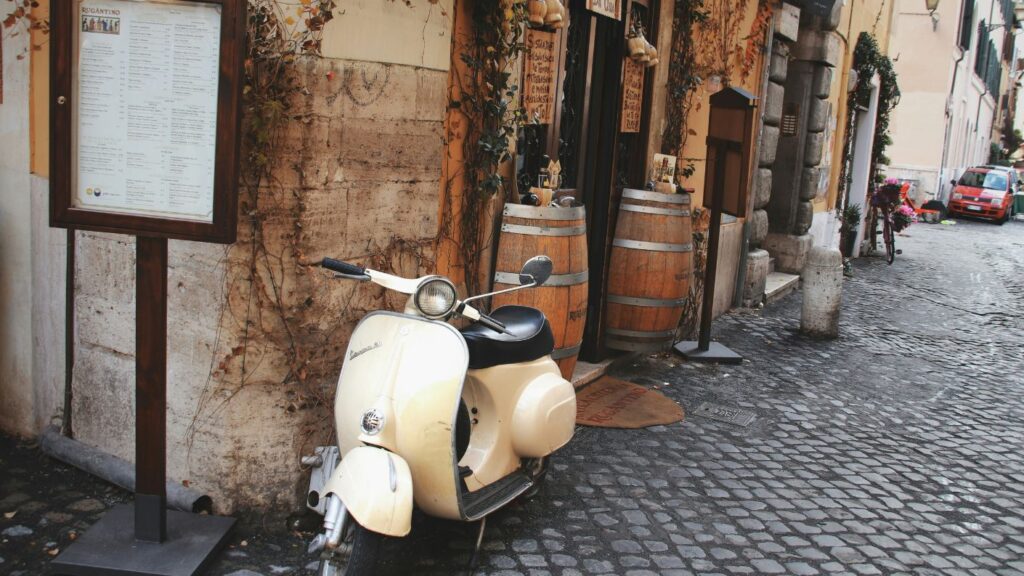 Veduta di un vicolo nel centro storico di Roma con vespa, san pietrini e botti