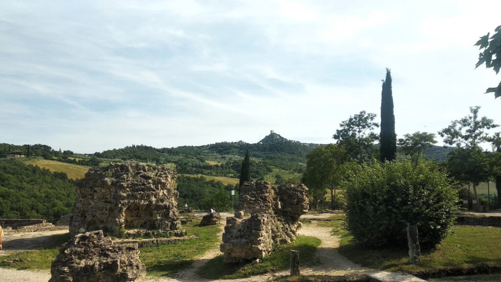 Rovine delle antiche terme di Bagno Vignoni con vista sulle colline della Val d'Orcia e Rocca d'Orcia sullo sfondo.