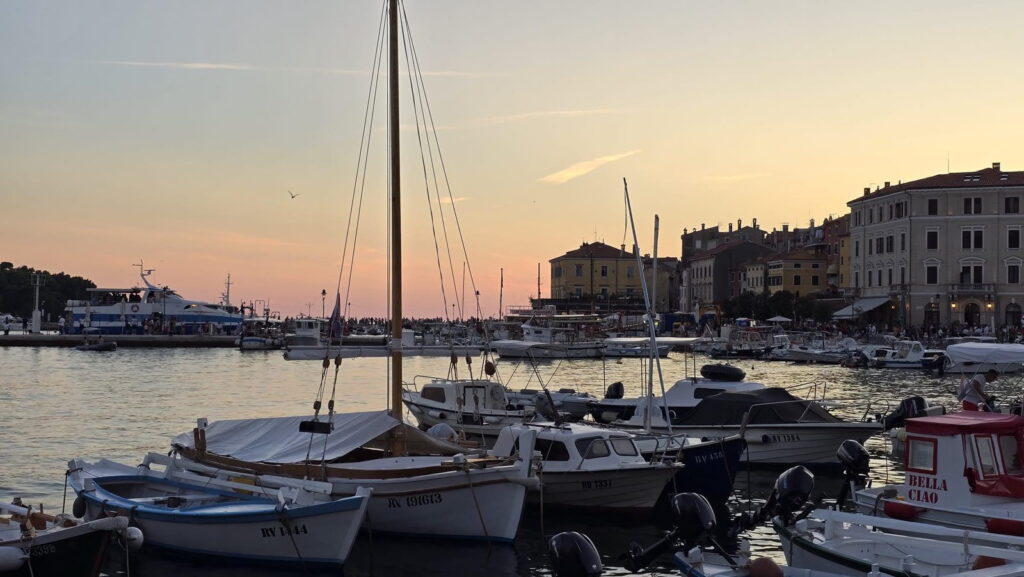 Veduta del porto di Rovigno, in Croazia, con barche sul mare al tramonto.