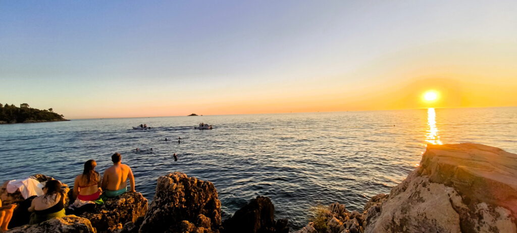 Veduta del tramonto sul mare e scogli con persone a Rovigno, in Croazia.